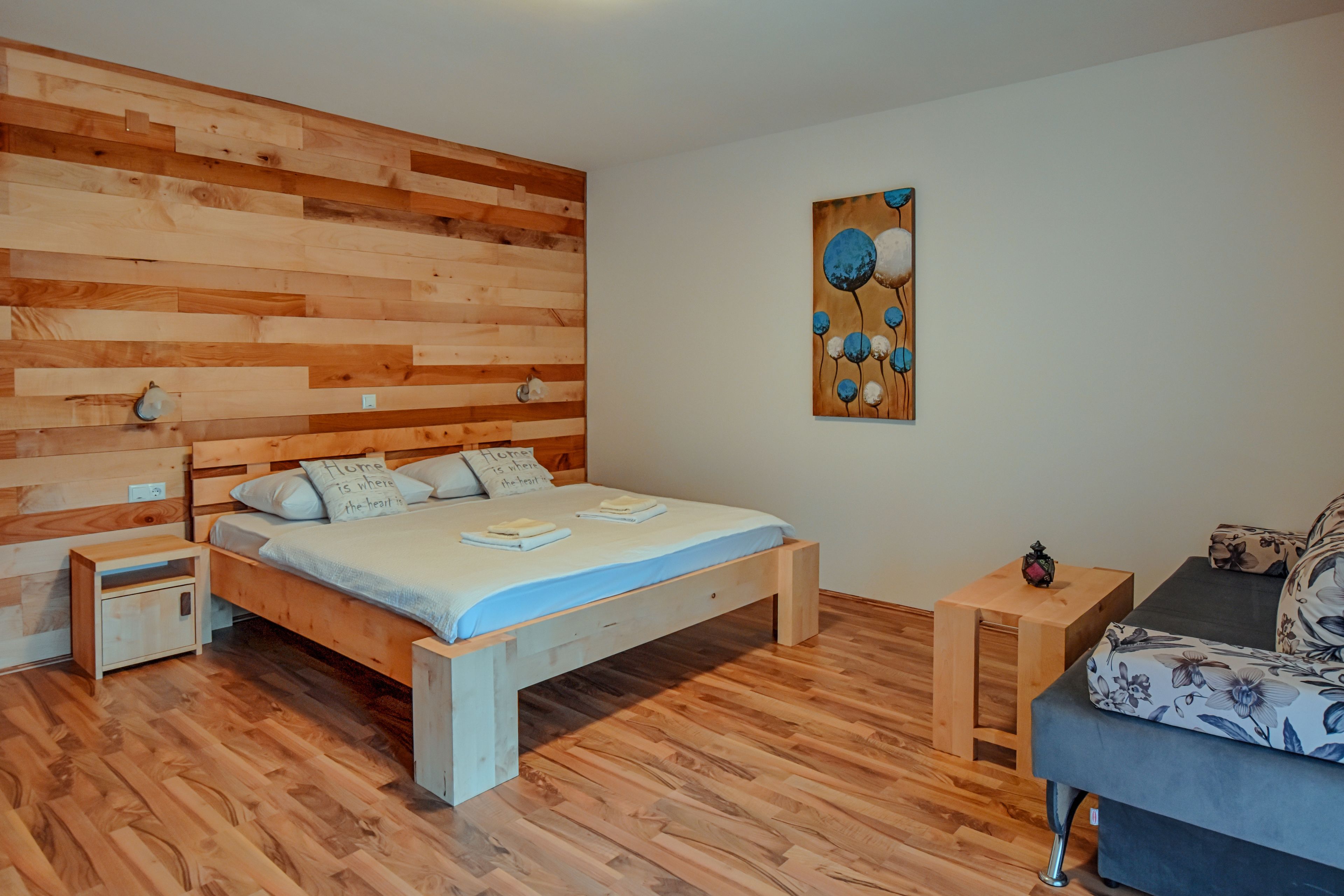 A bedroom with a wooden headboard, a bed with pillows, a nightstand, a small wooden table, and a sofa.