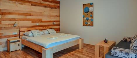 Un dormitorio con cabecera de madera, cama con almohadas, mesita de noche, pequeña mesa de madera y un sofá.
