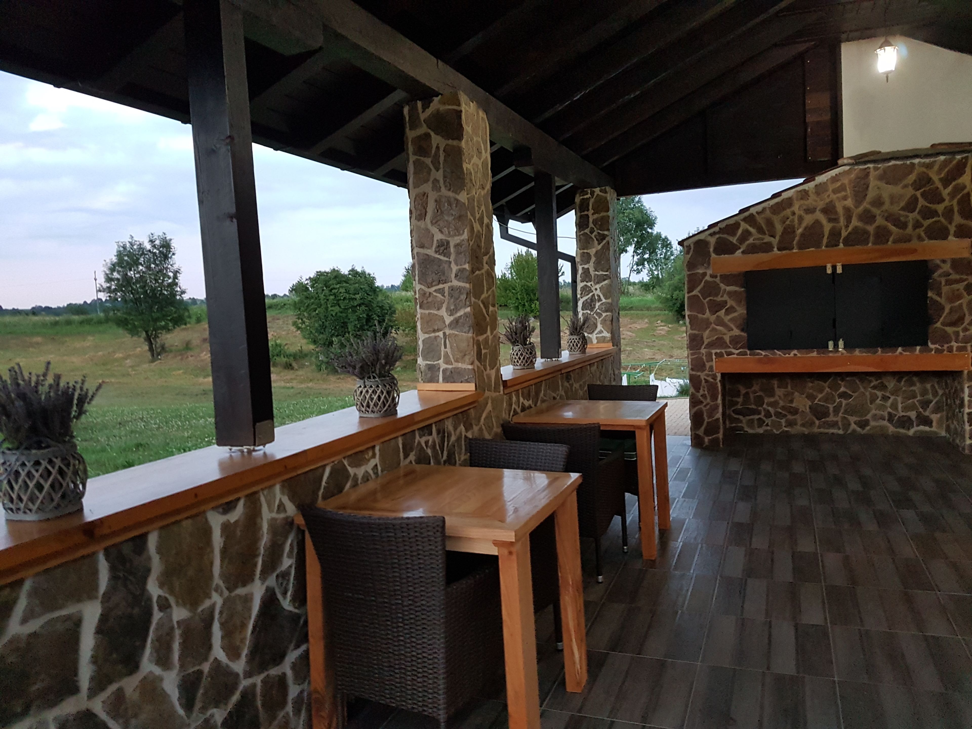 Eine Terrasse im Freien mit Steinpfeilern, Holztischen und einem eingebauten Grill.