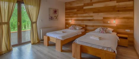 A room with two wooden beds, a wooden headboard, a large window with curtains, and a view of greenery outside.