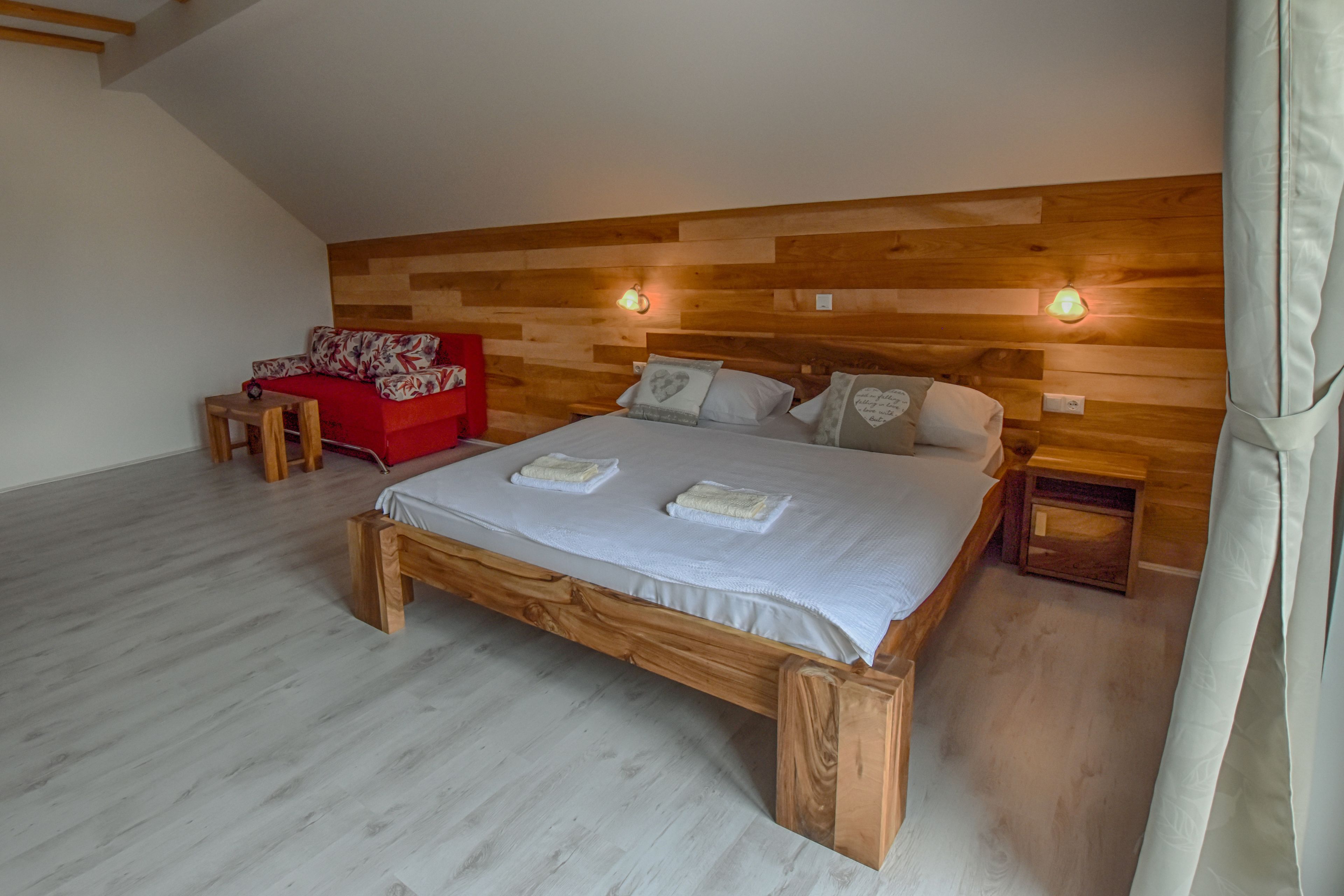 A bedroom with a wooden headboard, a red sofa, a wooden bed frame, and two bedside tables.