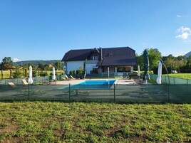 Una casa con piscina, rodeada por un área vallada con sillas de descanso y sombrillas.