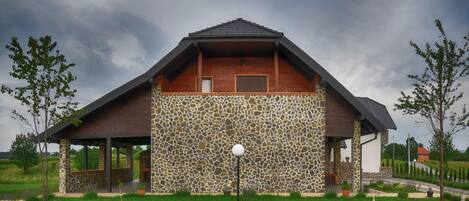 Un edificio moderno con fachada de piedra y techo de madera, rodeado de un césped cuidado y un camino pavimentado.