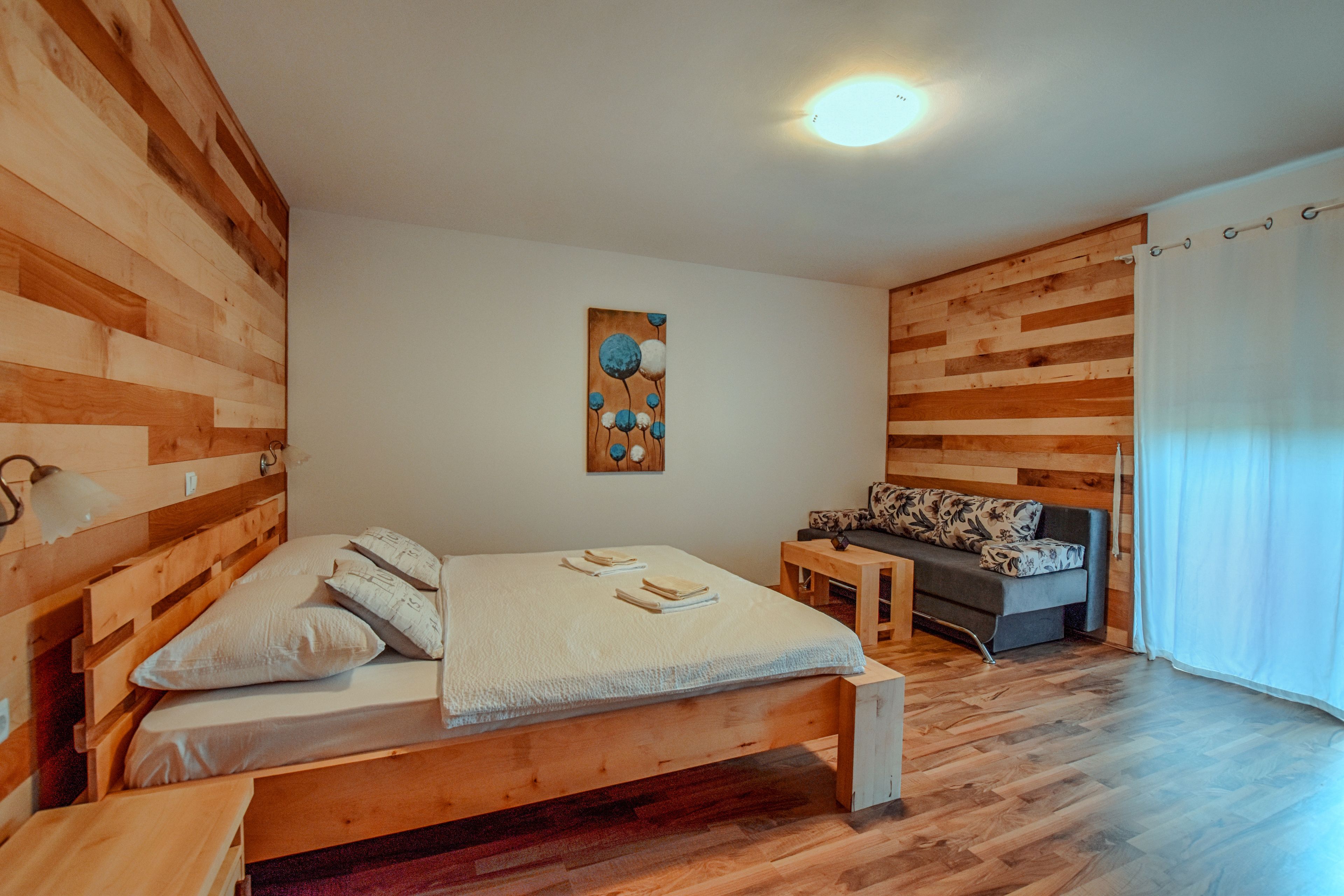 Een kamer met houten lambrisering, een bed, een bank, een tafeltje en een kunstwerk aan de muur.