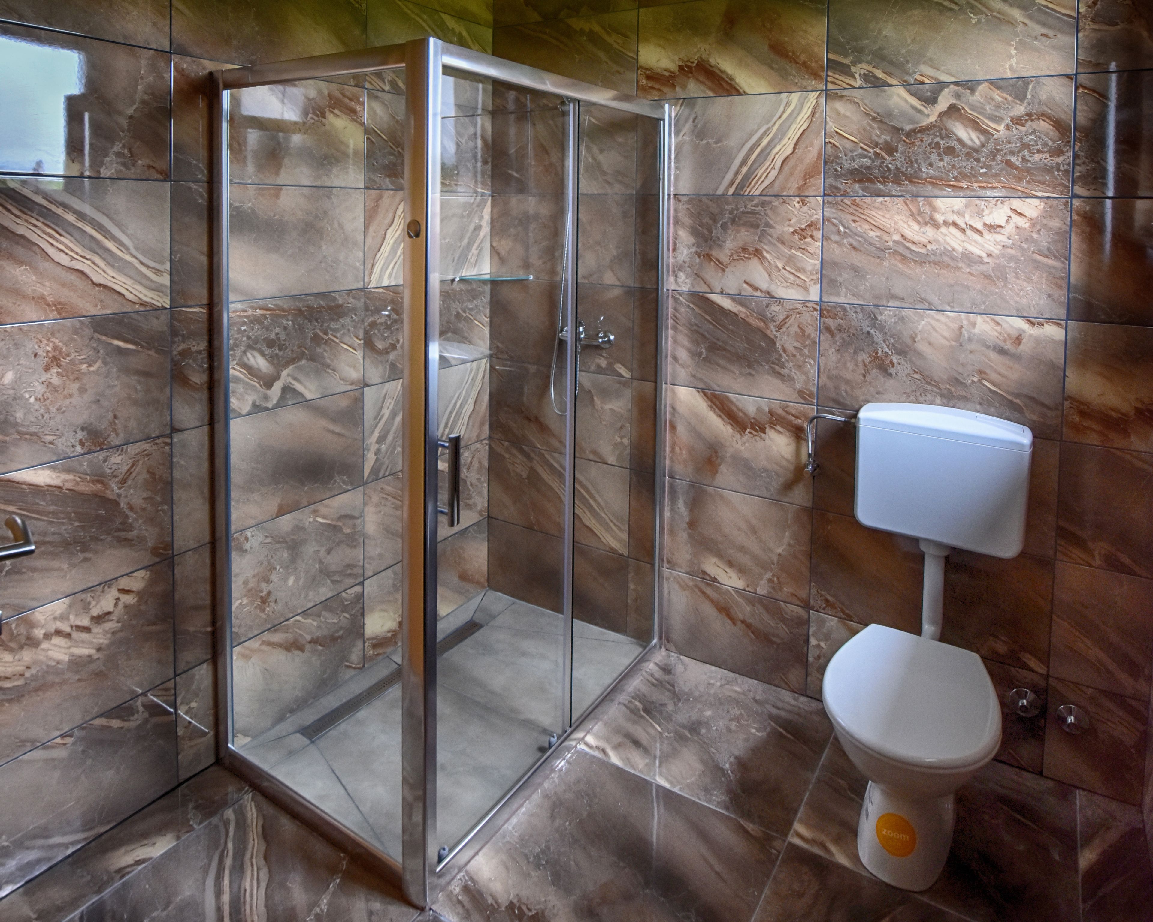 A bathroom with a glass shower enclosure, a toilet, and marble-patterned walls.