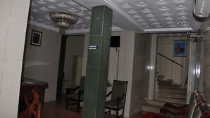 A reception area with a chandelier, a reception desk, and a staircase leading to an upper floor. - Hotel Magnificat (Lomé)