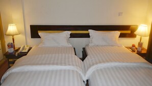 A hotel room with two beds, each with white bedding and a wooden headboard. There are bedside lamps and a telephone on the nightstands. - Hotel Magnificat (Lomé)