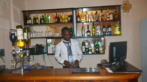 A bar area with shelves of liquor bottles, a bartender, and a computer monitor. - Hotel Magnificat (Lomé)