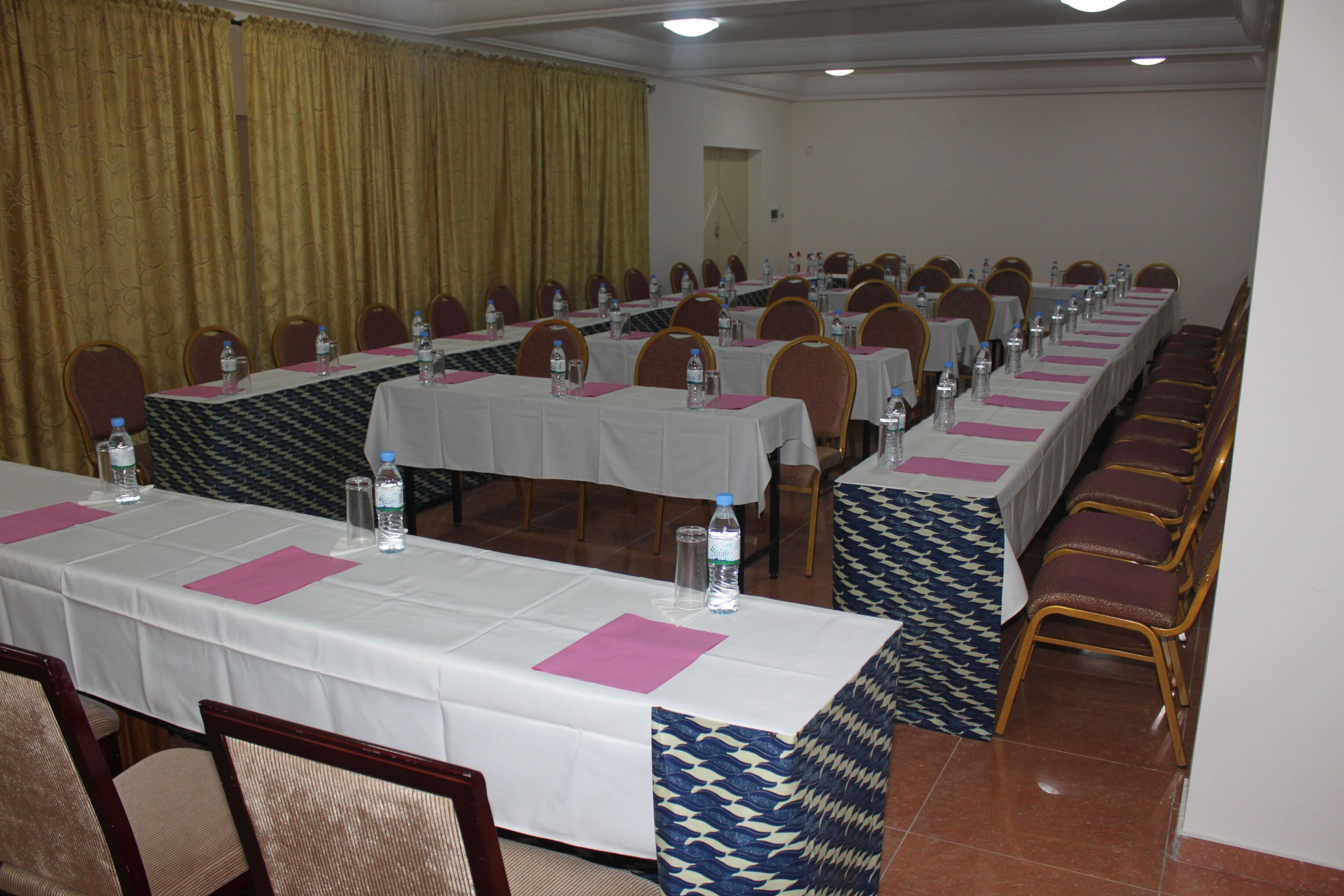 Uma sala de conferências com mesas grandes, cadeiras e garrafas de água.