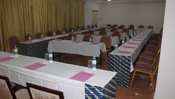 Uma sala de conferências com mesas grandes, cadeiras e garrafas de água.