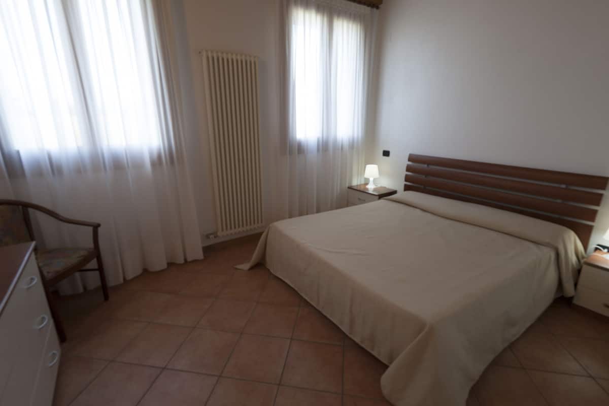 A bedroom with a bed, a nightstand, a chair, and a radiator.