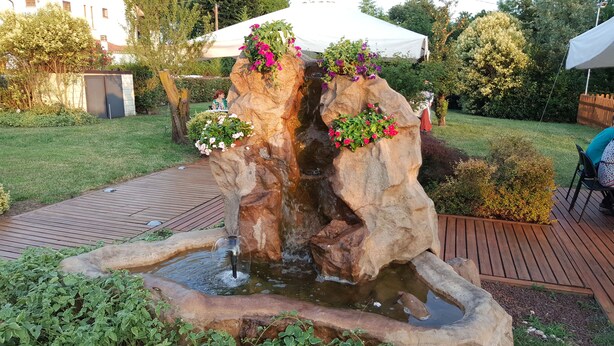Un jardín con una cascada de rocas, una terraza de madera y una tienda de campaña blanca.