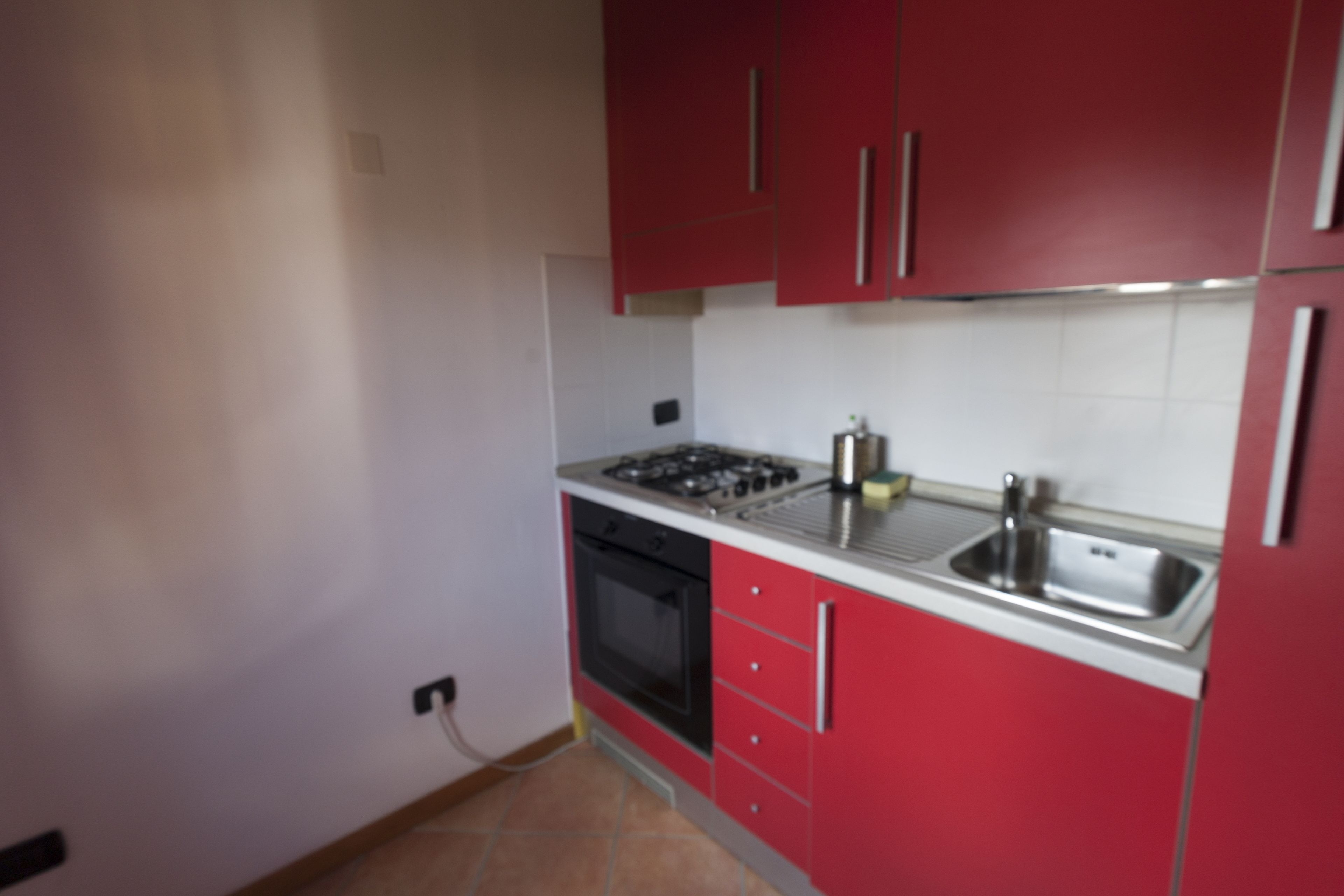 Une cuisine de taille réduite avec des meubles rouges, un évier en acier inoxydable et une cuisinière à gaz.