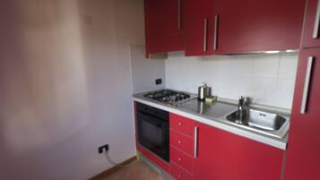 Une cuisine de taille réduite avec des meubles rouges, un évier en acier inoxydable et une cuisinière à gaz.