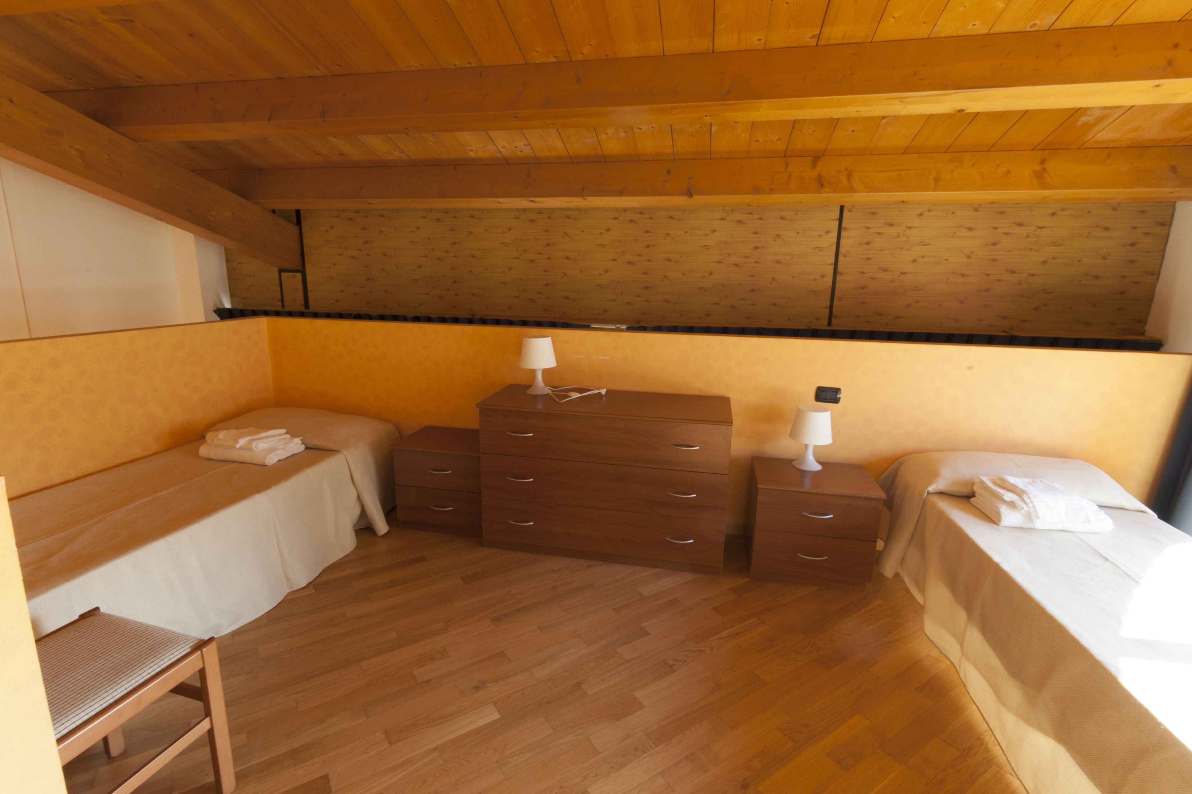 A small, cozy room with two single beds, a wooden dresser, and a small table.