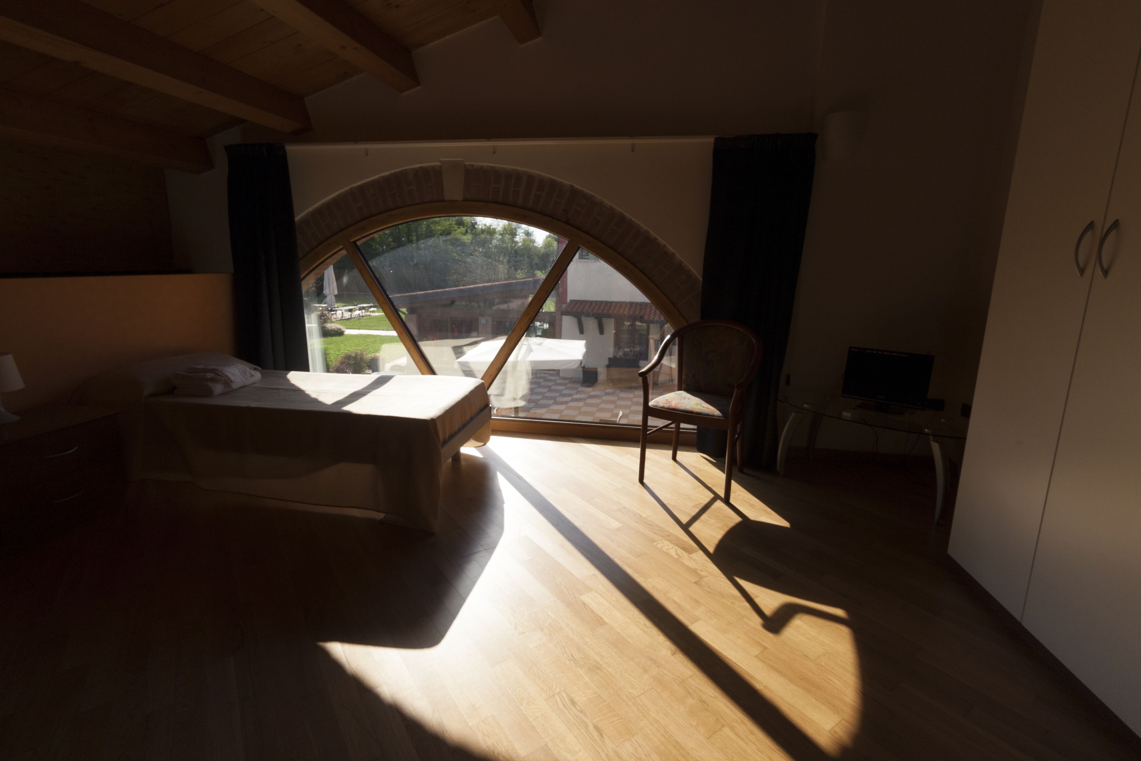 A room with a bed, a chair, a TV, and a view through a window.