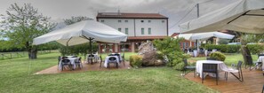 An outdoor dining area with tables and chairs, a wooden deck, and a building in the background. - Locanda Veneta (Vicenza)
