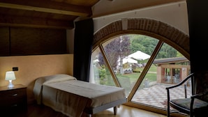 Un dormitorio con un amplio ventanal de arco, una cama, una mesita de noche y una silla.