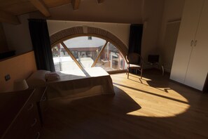 A spacious room with a large arched window, a bed, a chair, and a desk with a computer. - Locanda Veneta (Vicenza)