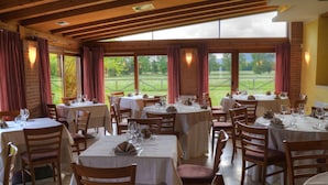 Un restaurante con mesas y sillas redondas, ventanas amplias y vistas al exterior.