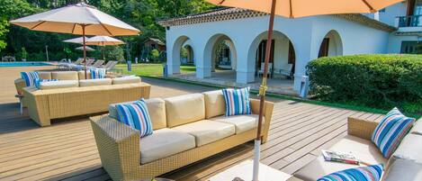 A wooden deck with outdoor furniture, including sofas and chairs, and umbrellas providing shade.