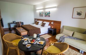 Ein Hotelzimmer mit Bett, Nachttisch, Lampe und einem Essbereich mit gedecktem Tisch für das Frühstück.