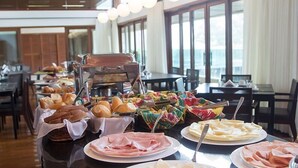 Een buffetopstelling met diverse gerechten, zoals brood, gebak en vleeswaren, in een goed verlicht eetgedeelte met grote ramen.