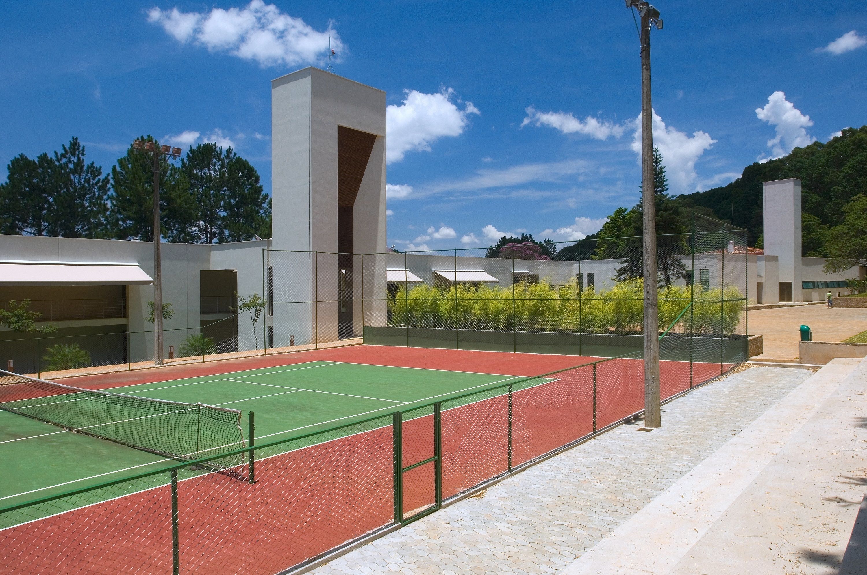 Een tennisbaan met een net, omringd door een hek, naast een gebouw met een modern architectonisch ontwerp.