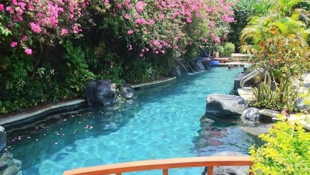 A clear pool with a wooden deck in the foreground, surrounded by lush greenery and pink flowers. - Poppies Bali Hotel (Kuta)