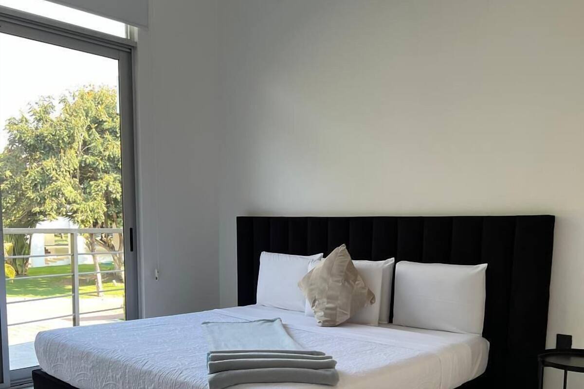 Ein modernes Schlafzimmer mit einem großen Bett, einem schwarzen Kopfteil und Blick ins Freie durch eine Schiebetür.