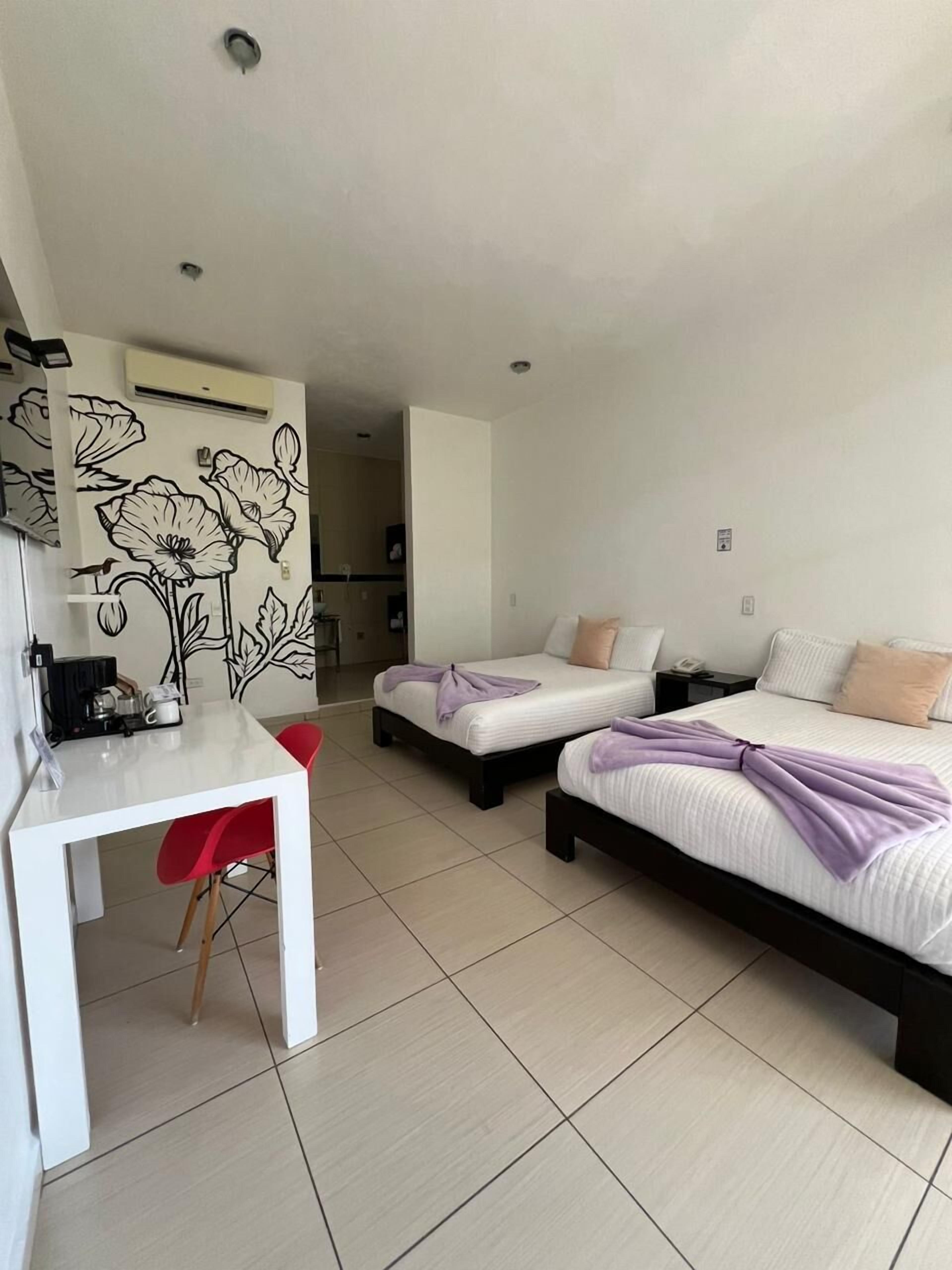 A hotel room with two beds, a small desk, and a kitchenette.