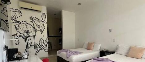 A hotel room with two beds, a small desk, and a kitchenette.
