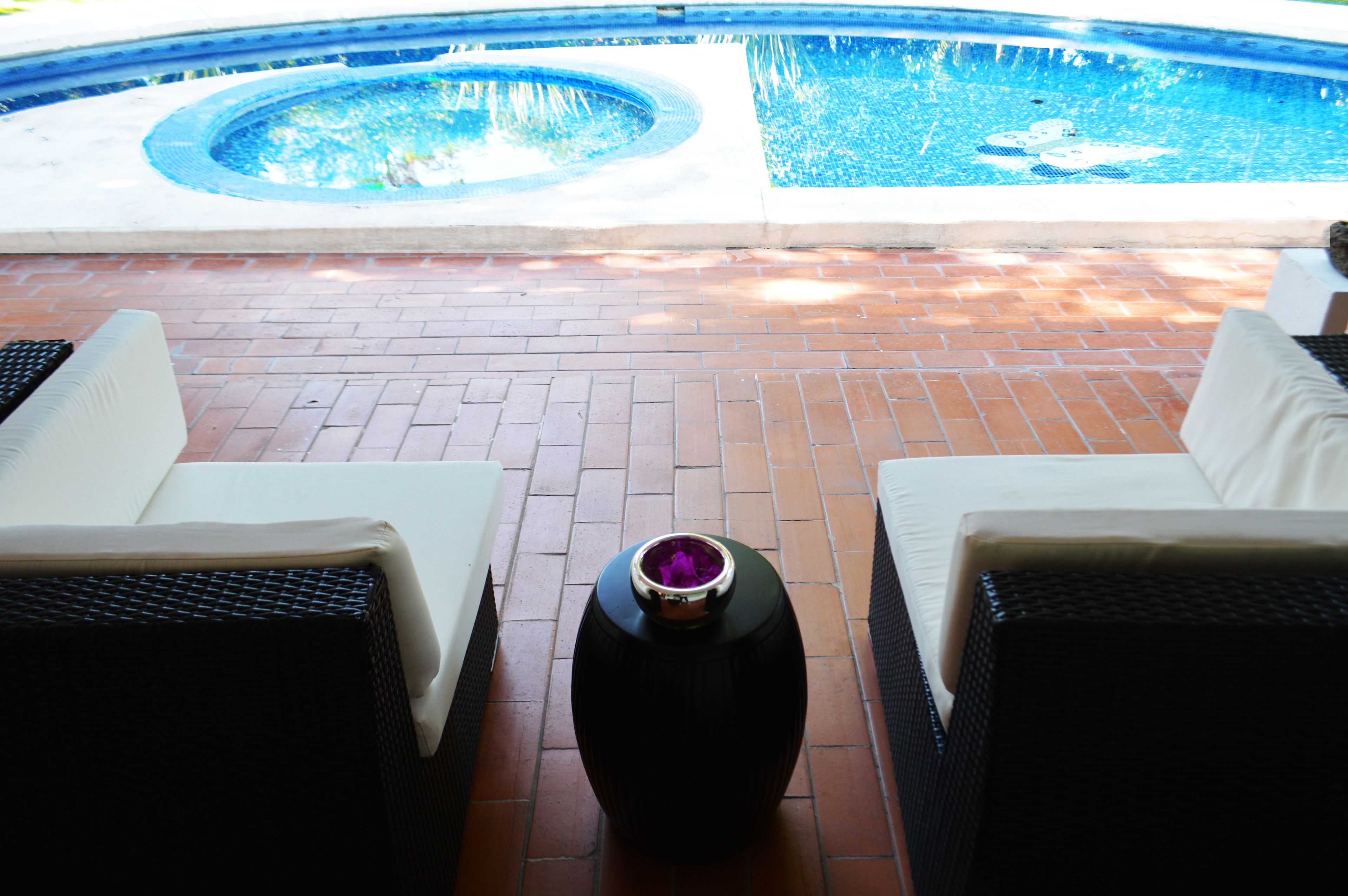 A poolside area with a hot tub, two white lounge chairs, and a decorative vase.