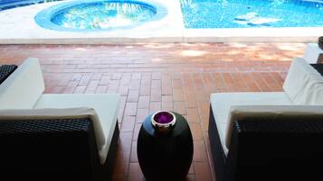 A poolside area with a hot tub, two white lounge chairs, and a decorative vase.