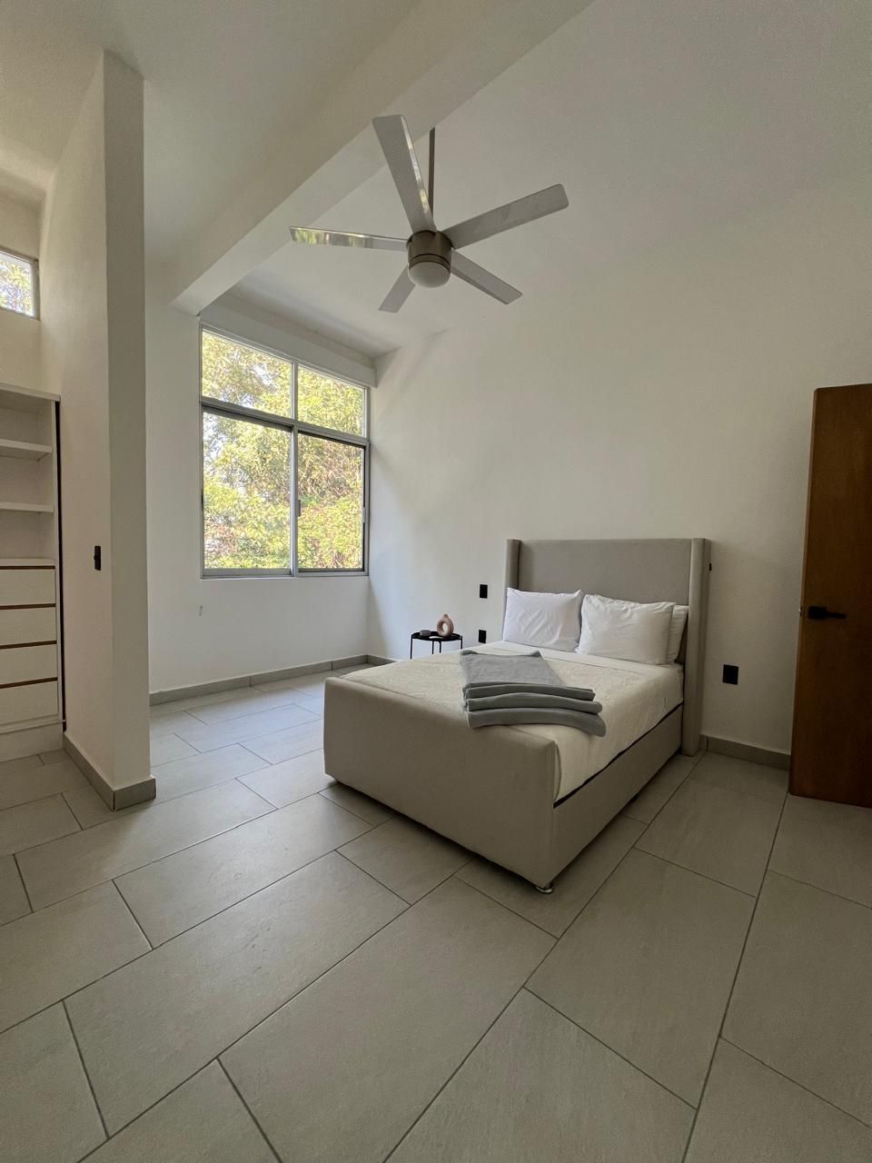 Une chambre à coucher avec un lit, un ventilateur de plafond, une fenêtre et une porte.