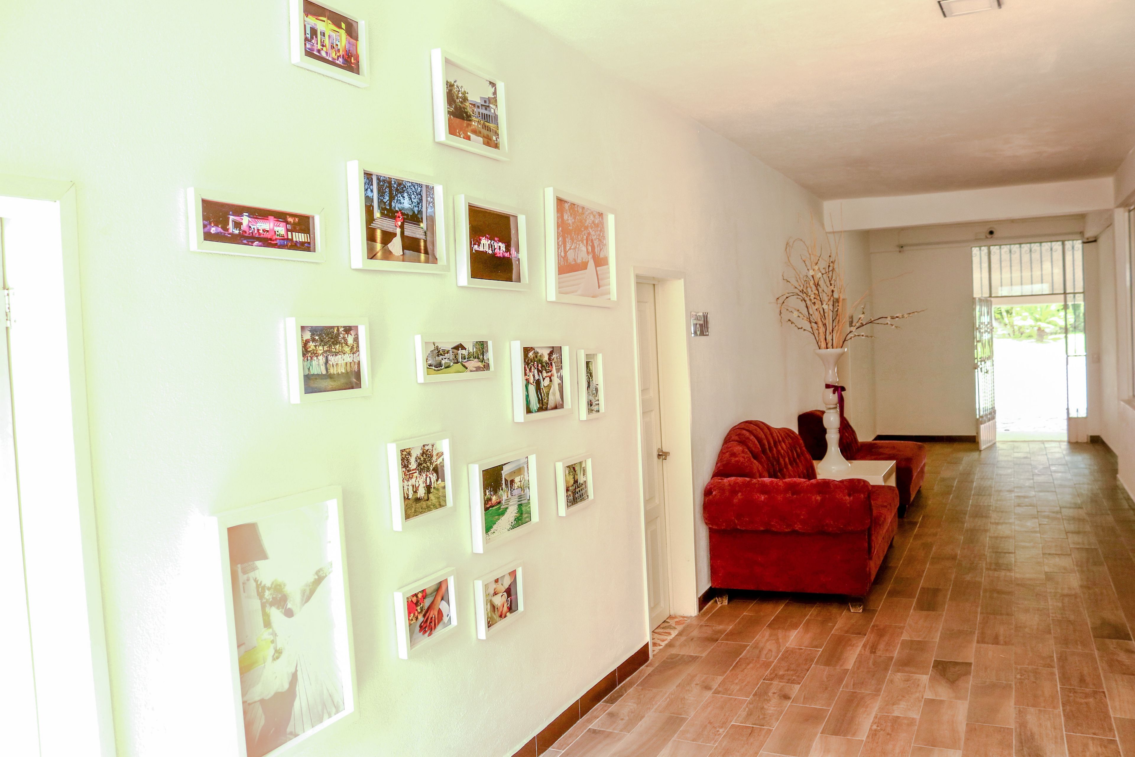 Amplia sala de estar con un sofá rojo, un jarrón blanco con ramas y una pared decorada con fotografías enmarcadas.