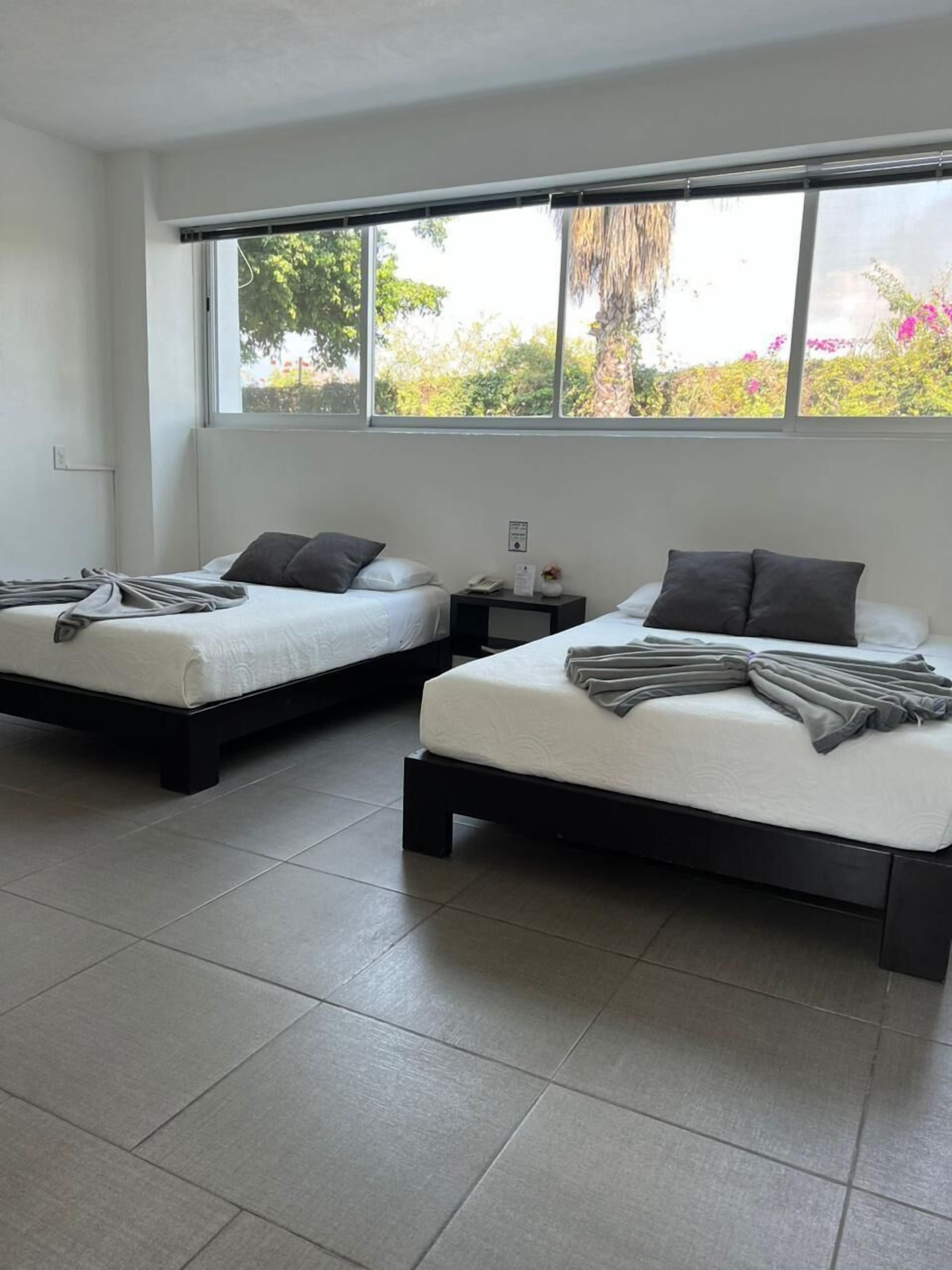 Una habitación de hotel moderna con dos camas individuales, un ventanal con vistas a zonas verdes y suelo de baldosas.