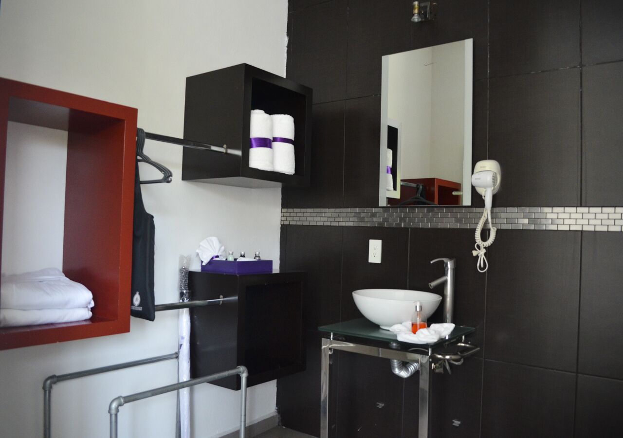 Een moderne badkamer met een zwart betegelde muur, een witte wastafel, een spiegel en een handdoekhouder.