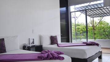 Habitación de hotel moderna con dos camas, un ventanal grande y un balcón con vistas a zonas verdes.