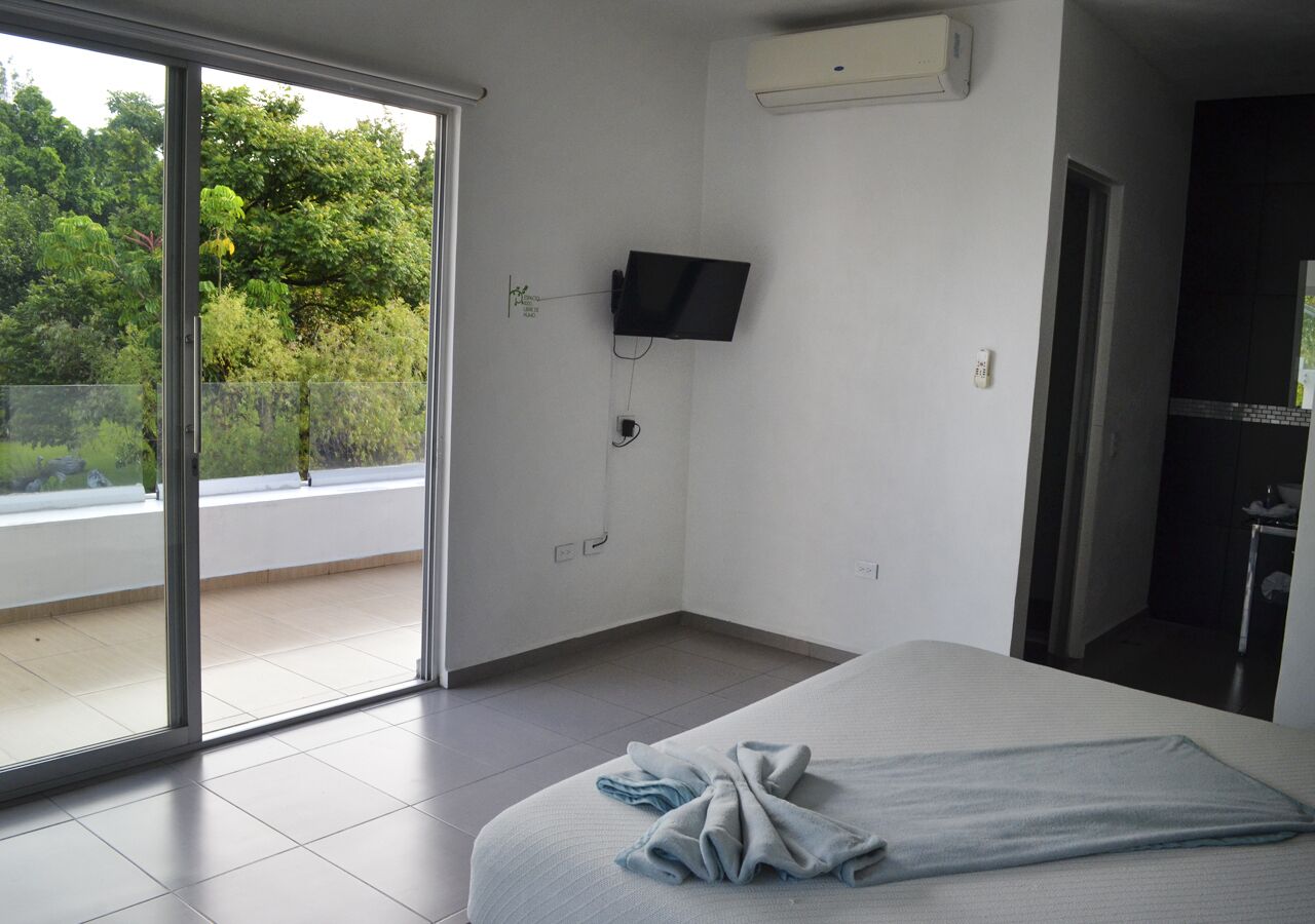 Ein Hotelzimmer mit Bett, Wandfernseher und einer Schiebetür zu einem Balkon mit Blick ins Grüne.