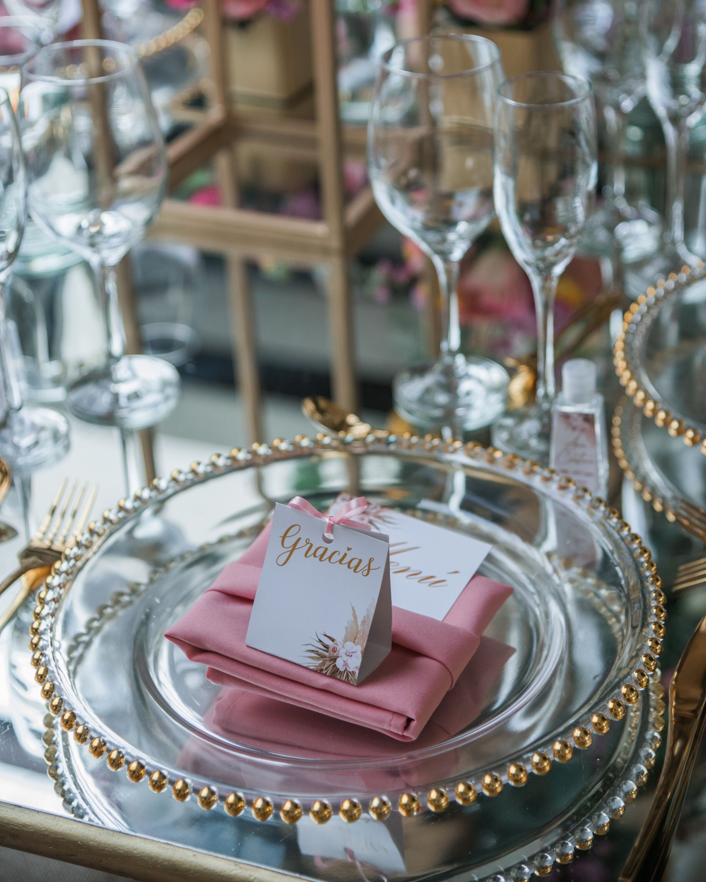 Ein Tisch, gedeckt mit klarem Glas, einem rosa Servietten und einem Schild mit der Aufschrift 'Gracias'.