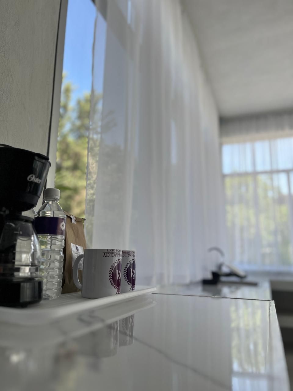 Una encimera de cocina con una cafetera, una botella de agua, una bolsa de papel y dos tazas.