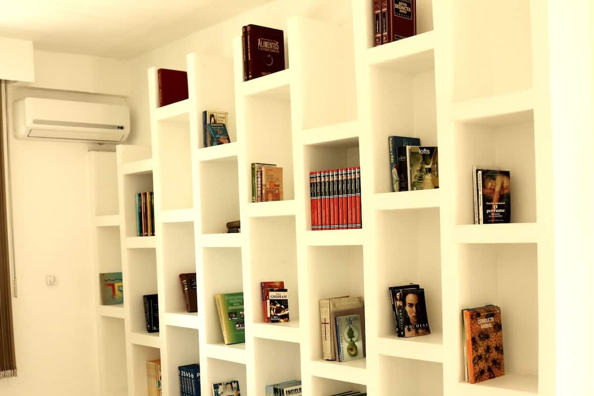 Ein Hotelzimmer mit einem weißen Bett, einer Bücherwand voller Bücher und einem gefliesten Boden.