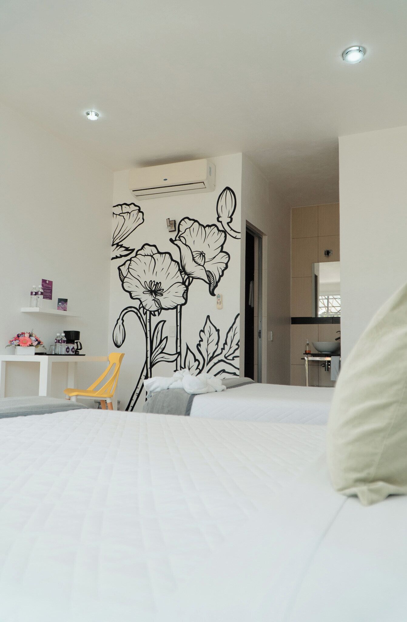 A hotel room with a bed, a chair, a desk with a computer, and a wall with a floral decal.