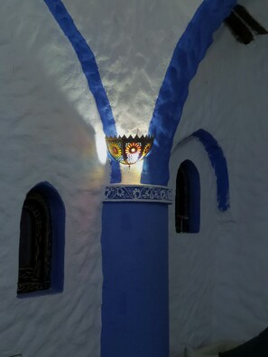 A building with white walls and blue accents, featuring a decorative light fixture and arched windows. - Riad Antek (Chefchaouen)
