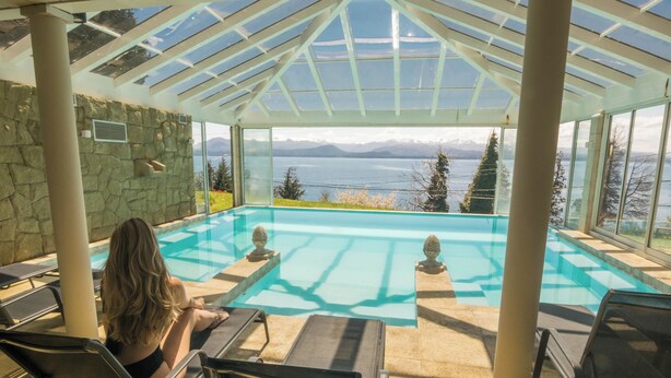 A pool area with a glass ceiling, stone walls, and a view of mountains. - Pailahue Lodge & Cabañas (San Carlos de Bariloche)