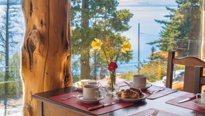 A table set for breakfast with a view of the sea, a vase with flowers, and a wooden table. - Pailahue Lodge & Cabañas (San Carlos de Bariloche)