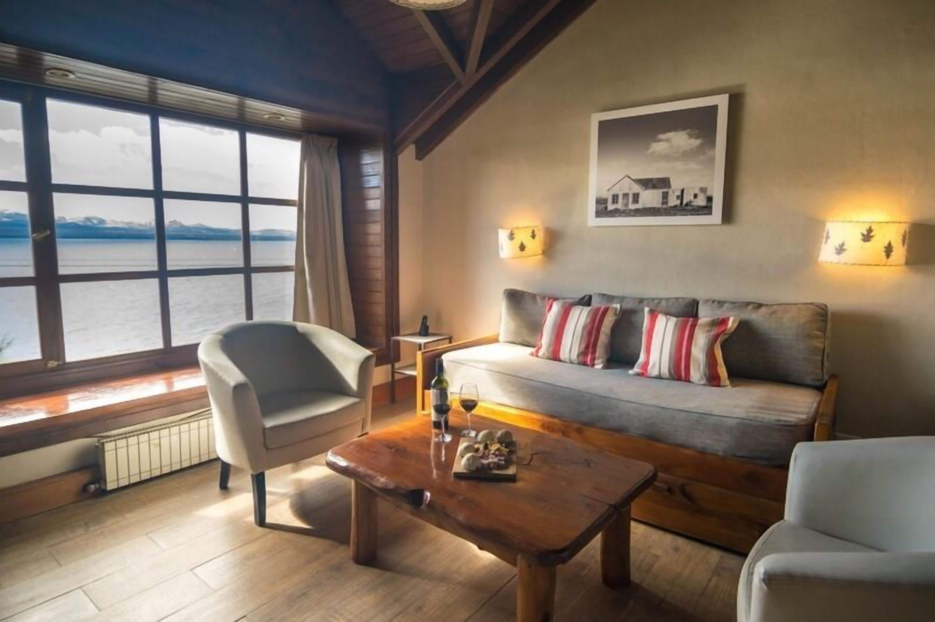 Een gezellige kamer met een bank, twee stoelen, een houten salontafel en uitzicht op het water door grote ramen.