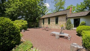 Ein Steinhaus mit Kiesterrasse, Sitzgelegenheiten im Freien und üppigem Grün.