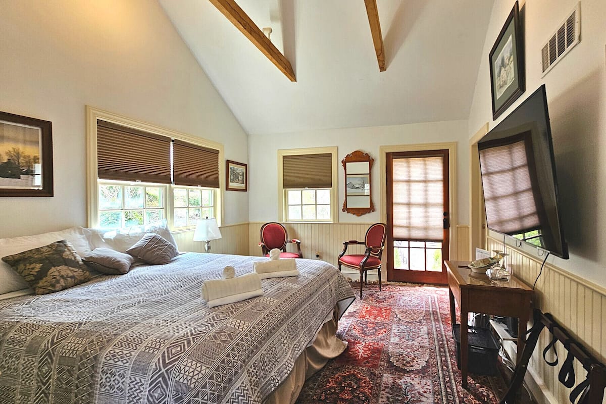 A bedroom with a bed, two chairs, a TV, and a window with blinds.